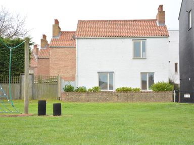A backyard with a grass lawn and climbing structure in front of houses with tiled roofs and brick walls at Sweet Pea Southwold