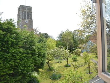 A garden with trees and grass and a stone clock tower visible in the background at Sweet Pea Southwold