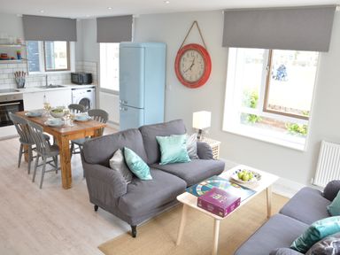 An open plan living and kitchen area with sofas and a coffee table next to a dining table set for four at Sweet Pea Southwold