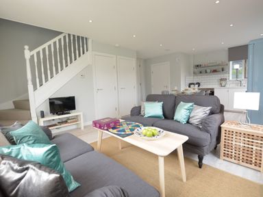A living room with sofas cushions a coffee table with a board game and a bowl of apples a television and kitchen area at Sweet Pea Southwold