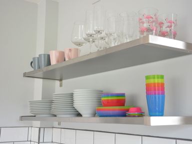 Two metal kitchen shelves with cups, wine glasses, plates, bowls, and colorful plastic cups and bowls at Sweet Pea Southwold