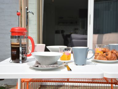 A table set with a French press coffee maker cups bowls glasses with orange juice and a plate of croissants at Sweet Pea Southwold