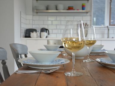 A kitchen dining table set with bowls plates napkins and glasses of white wine at Sweet Pea Southwold