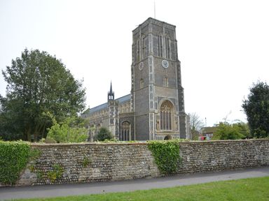 Exterior view of a stone church with a tall tower and clock behind a stone wall with greenery