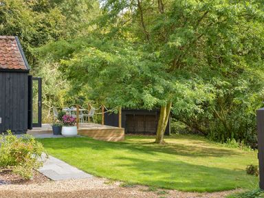 A garden with a tree and a wooden deck with outdoor furniture at Spexhall Barns in Halesworth