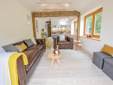 A living room with brown leather sofas, a wooden beam, and large windows at Spexhall Barns in Halesworth
