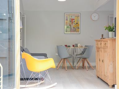A dining room with gray chairs around a table and a yellow rocking chair near a wooden cabinet at Spexhall Barns in Halesworth