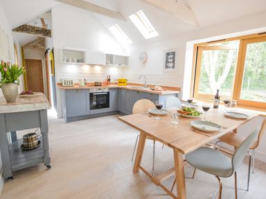 A kitchen with a wooden dining table set for four and blue lower cabinets at Spexhall Barns in Halesworth