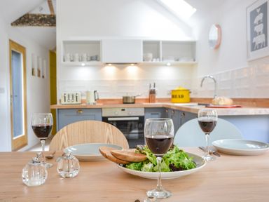 A kitchen with plates glasses of wine a bowl of salad and cutting boards on a wooden table at Spexhall Barns in Halesworth
