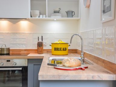 A kitchen counter with a loaf of bread on a cutting board next to a sink with a chrome faucet and a yellow bread container at Spexhall Barns in Halesworth