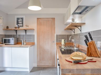 A kitchen with wooden countertops a loaf of bread on a cutting board a knife set a microwave kettle and a wooden door at Spexhall Barns in Halesworth