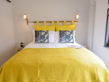 A bedroom with a bed with yellow pillows and blanket and two wall-mounted lamps at Spexhall Barns in Halesworth