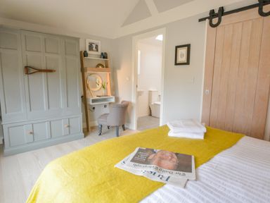 A bedroom with a bed a yellow blanket a gray wardrobe a chair a desk and a bathroom visible at Spexhall Barns in Halesworth