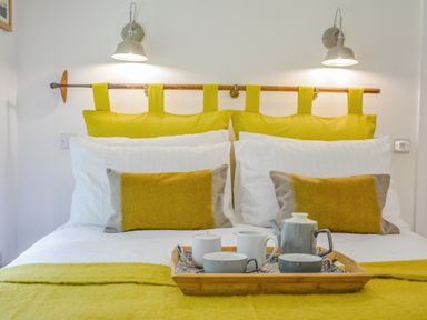 A bed with white sheets yellow pillows and a tray with a teapot cups and a sugar bowl at Spexhall Barns in Halesworth
