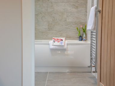 A bathroom with a white bathtub towels a book on the tub edge and flowers in vases at Spexhall Barns in Halesworth