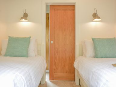 A bedroom with two single beds a wooden sliding door and wall lights at Spexhall Barns in Halesworth