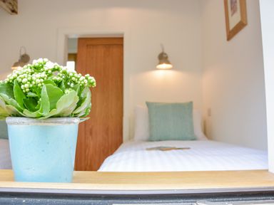 A bedroom with a bed pillow and wall lamps with a blue potted plant in the foreground at Spexhall Barns in Halesworth