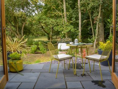 A patio with two chairs and a table with a book and cup surrounded by plants and trees at Spexhall Barns in Halesworth
