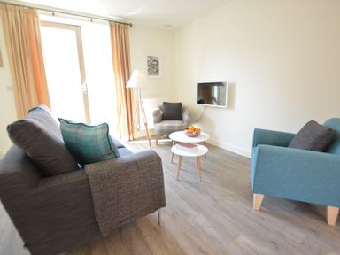 A living room with sofas armchair coffee tables and a wall-mounted tv at Mycroft Southwold in Southwold