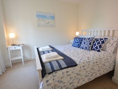 A bedroom with a bed with white and blue bedding and pillows two bedside tables with lamps and a painting on the wall at Mycroft Southwold in Southwold