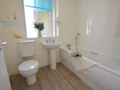 A bathroom with a toilet sink bathtub flowers on the window sill at Mycroft Southwold in Southwold
