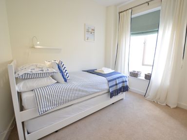 A bedroom with a single bed with striped bedding and pillows next to a window with curtains and a roman blind at Mycroft Southwold in Southwold