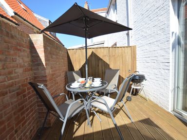 An outdoor patio with a round glass table set with bowls and plates surrounded by four chairs and a large umbrella at Mycroft Southwold in Southwold