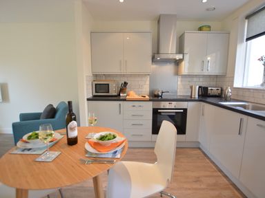 A kitchen with white cabinets a wooden dining table with plates glasses of wine and a bottle at Mycroft Southwold in Southwold