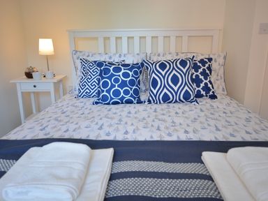 A bed with blue and white pillows and patterned bedding with folded white towels on a navy blanket at Mycroft Southwold in Southwold