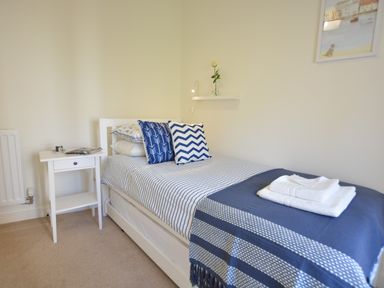 A single bed with blue and white bedding next to a white bedside table with a candle and magazines at Mycroft Southwold in Southwold