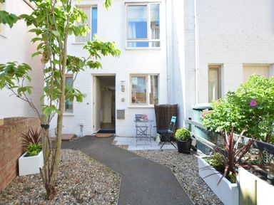 A small courtyard with a pathway leading to a white brick house with outdoor seating and potted plants at Mycroft Southwold in Southwold