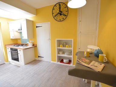 A kitchen with a stove oven combination a table with mugs and a teapot and a wall clock at Alinka Aldeburgh in Aldeburgh
