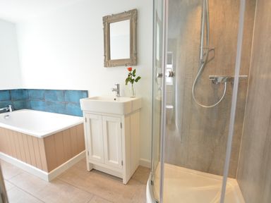A bathroom with a bathtub with blue tiles a white vanity with a mirror and a shower with glass doors at Alinka Aldeburgh in Aldeburgh