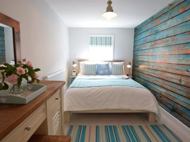 A bedroom with a bed against a blue wooden paneled wall and a wooden dresser with flowers on it at Alinka Aldeburgh in Aldeburgh