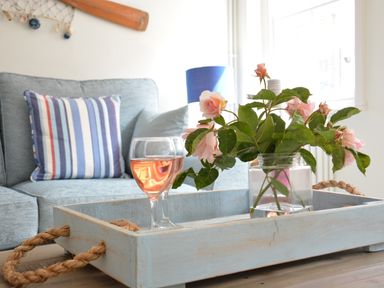 A living room with a blue sofa two pillows a wooden tray holding a vase of pink flowers and a glass of pink drink at Alinka Aldeburgh in Aldeburgh