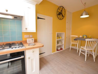 A kitchen with white cabinets a wooden countertop a gas stove a small table with two chairs and yellow walls at Alinka Aldeburgh in Aldeburgh