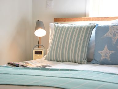 A bed with striped and starfish pillows a folded newspaper and a bedside lamp at Alinka Aldeburgh in Aldeburgh