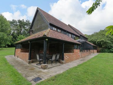 An outdoor patio area with a table and chairs next to a brick and wood house surrounded by grass and trees at Quill Farm Barn in Campsea Ashe