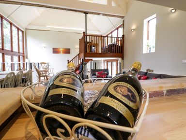 A living area with two bottles of prosecco in a basket on a wooden counter and wooden furniture at Quill Farm Barn in Campsea Ashe