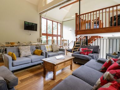 A living room with grey sofas a wooden coffee table dining table with chairs and wooden railings at Quill Farm Barn in Campsea Ashe