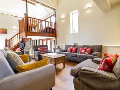 A living room with multiple sofas around a wooden coffee table and a wooden staircase with a loft area at Quill Farm Barn in Campsea Ashe