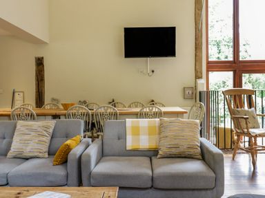 A living area with gray sofas and patterned cushions in front of a dining table with chairs and a wall-mounted TV at Quill Farm Barn in Campsea Ashe
