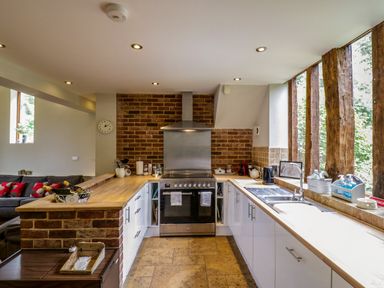 A kitchen with wooden countertops white cabinets a stove and a sink next to windows with wooden beams at Quill Farm Barn in Campsea Ashe