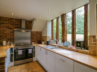 A kitchen with a stove sink wooden countertops and large vertical windows at Quill Farm Barn in Campsea Ashe