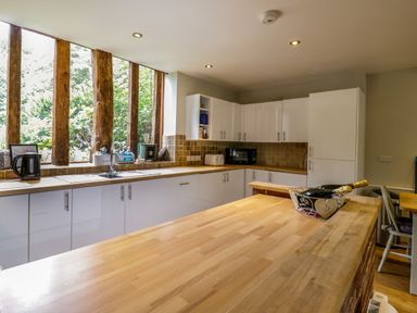 A kitchen with wood countertops white cabinets and large windows with wooden beams at Quill Farm Barn in Campsea Ashe