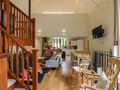 An open plan living area with wooden stairs dining table chairs sofas and a wall mounted television at Quill Farm Barn in Campsea Ashe