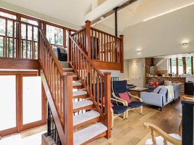 A living area with wooden staircase chairs sofas and kitchen at Quill Farm Barn in Campsea Ashe