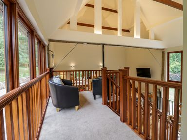 A balcony area with two black armchairs and wooden railings overlooking a living area at Quill Farm Barn in Campsea Ashe