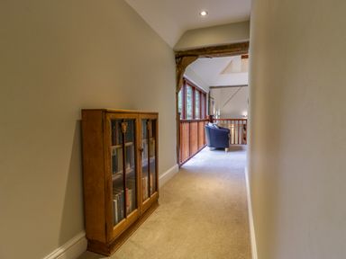 A hallway with a wooden cabinet of books and a seating area with a chair at Quill Farm Barn in Campsea Ashe