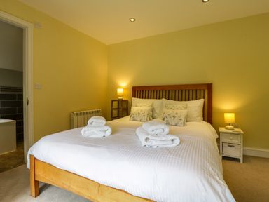 A bedroom with a wooden bed and white bedding with rolled towels and bedside tables with lamps at Quill Farm Barn in Campsea Ashe